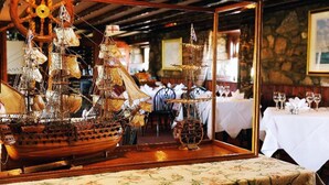 Un modelo de barco sobre una mesa en un restaurante, con una pared de piedra y fotografías enmarcadas al fondo.