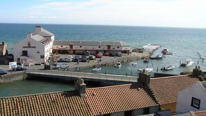 Un edificio costero con techo de tejas, zona de estacionamiento y barcos amarrados en el agua.