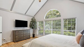 Ein Schlafzimmer mit Bett, Schminktisch, Fernseher und großen Fenstern mit Jalousien.