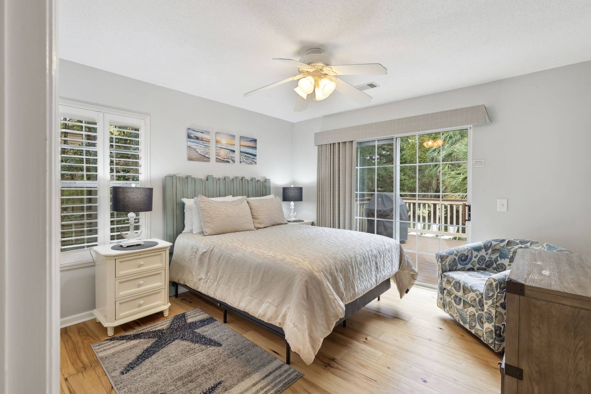 A bedroom with a bed, nightstands, a desk, a chair, a ceiling fan, and large windows.