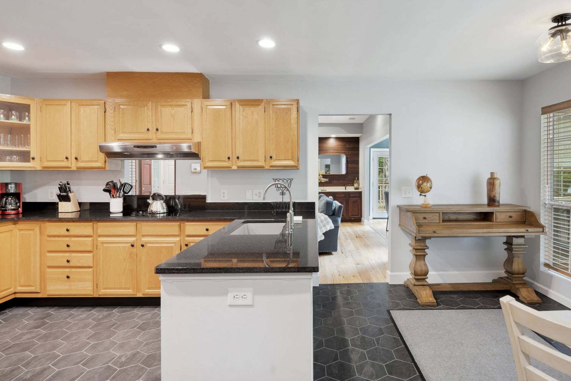 A modern kitchen with wooden cabinets, a black countertop, and a central island. There is a dining area with a wooden table and chairs.