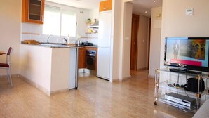 Una cucina moderna con isola centrale, zona pranzo con una sedia e soggiorno con televisore e impianto stereo.