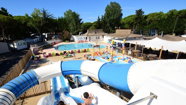 Parque acuático con toboganes y piscinas, rodeado de árboles y edificios.