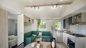 Cocina compacta con electrodomésticos modernos, comedor con mesa y sillas, y un sofá verde en una habitación luminosa con luz natural.