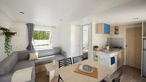 Un espacio habitable moderno y compacto con sofá, mesa de comedor y kitchenette.