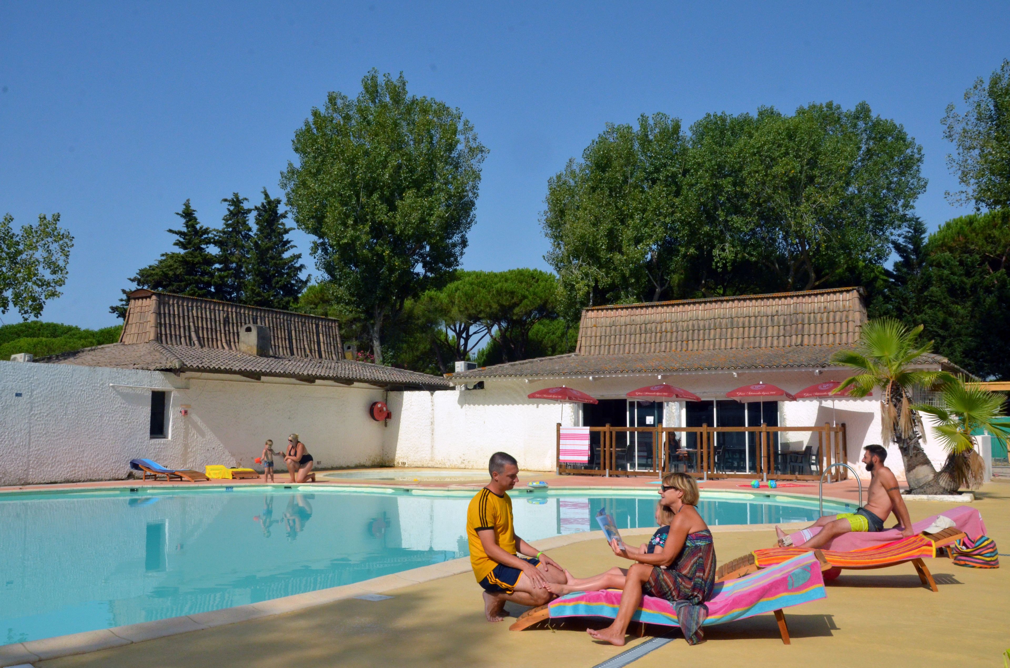 Zona de piscina con sillones de descanso, un bar junto a la piscina y un edificio con tejado de tejas.