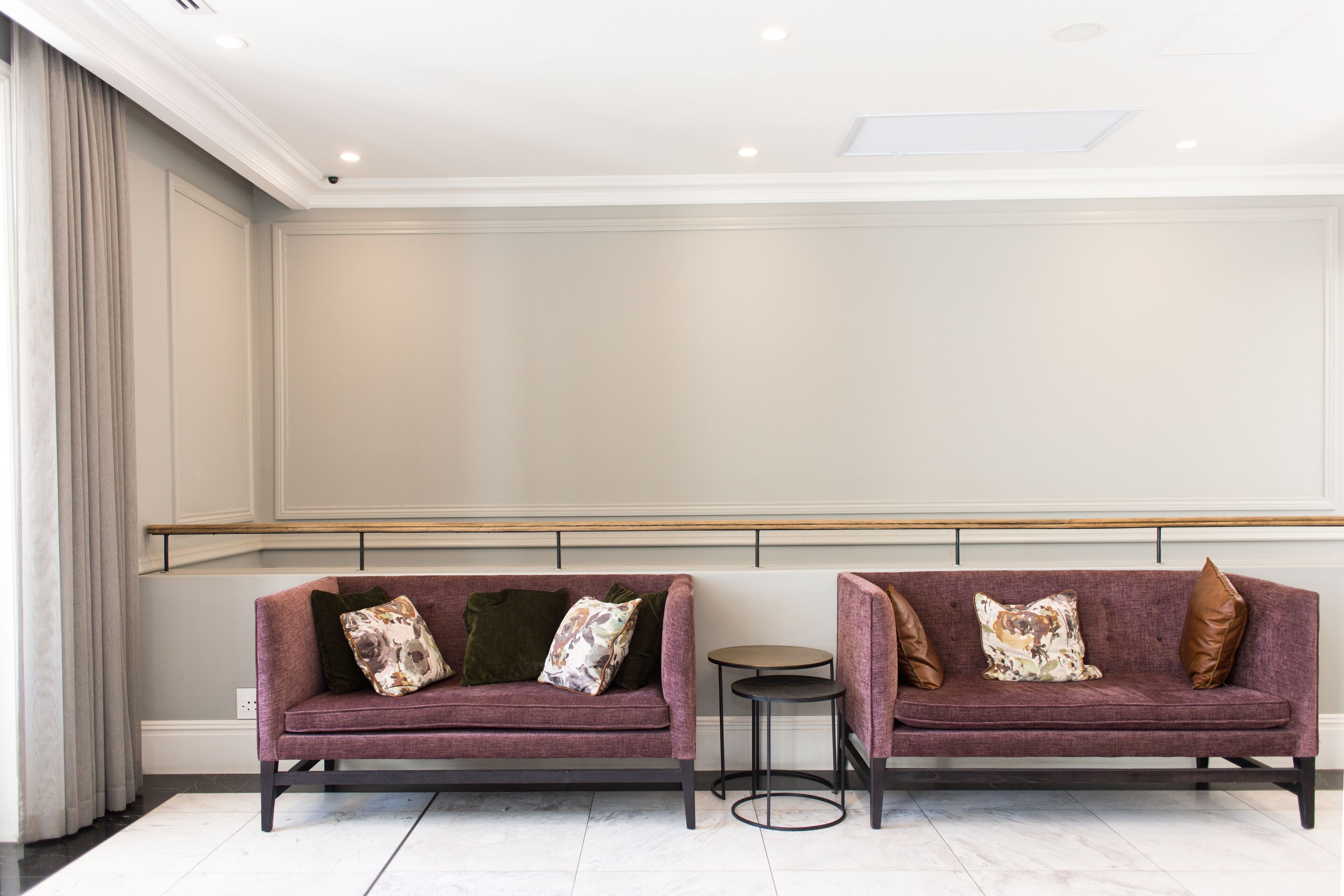 Two purple sofas with decorative pillows, a small round table, and a white wall with a wooden bench.