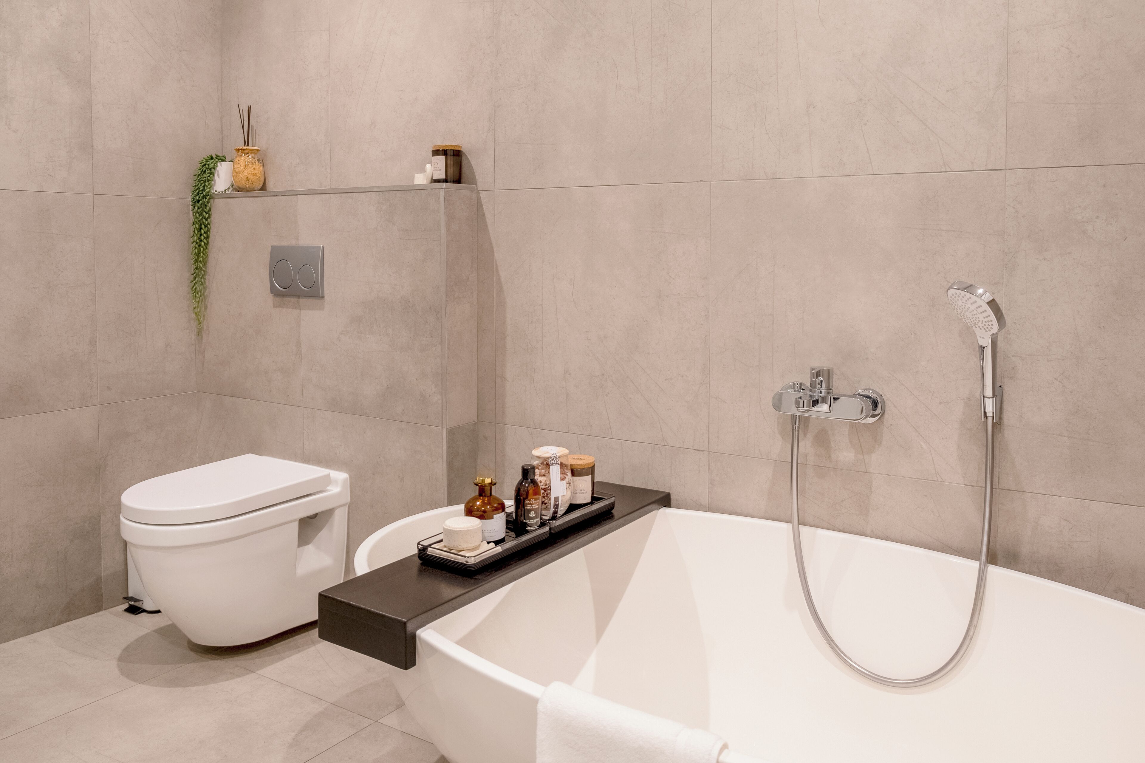 Ein modernes Badezimmer mit Toilette, einer Badewanne mit Duschkopf und einem Ablagefach für Pflegeprodukte.