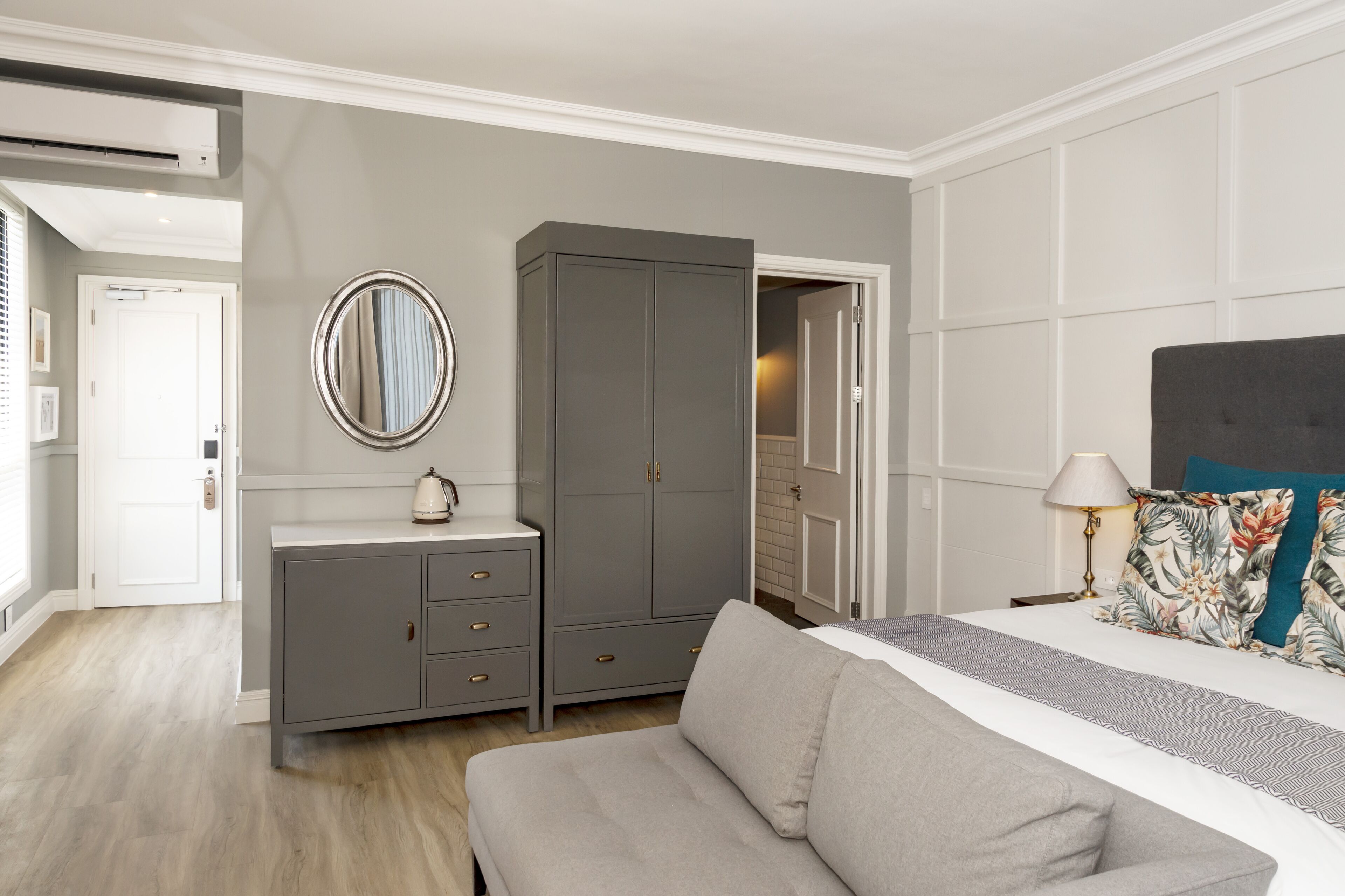 A bedroom with a bed, grey wardrobe, bedside table, and a mirror.