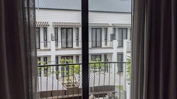 A view through a sliding glass door to a balcony with a white building in the background, featuring a striped awning and a metal railing.