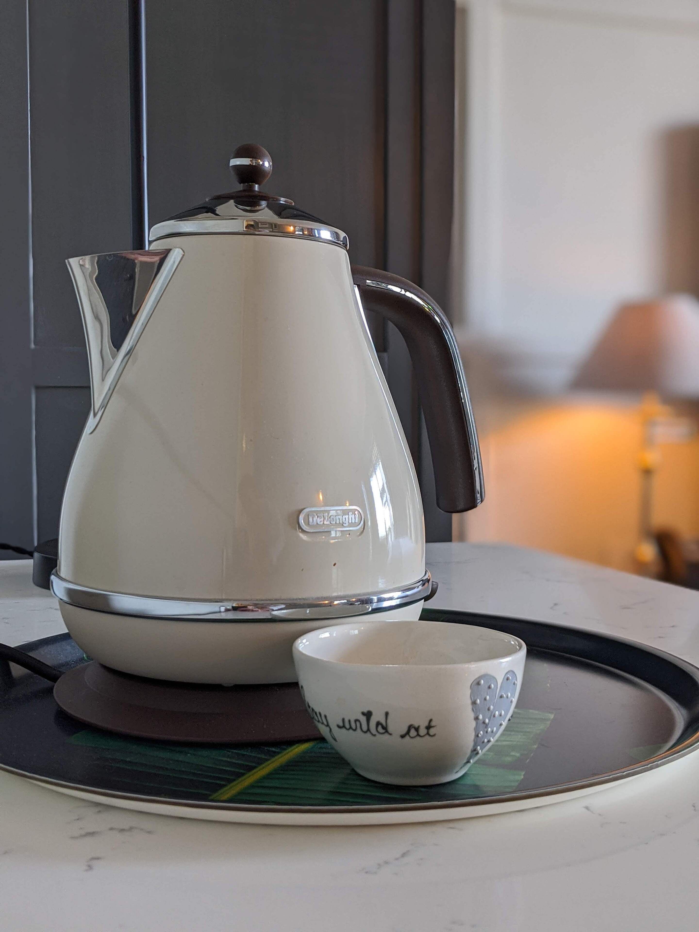 A white electric kettle with a lid and handle, placed on a tray.