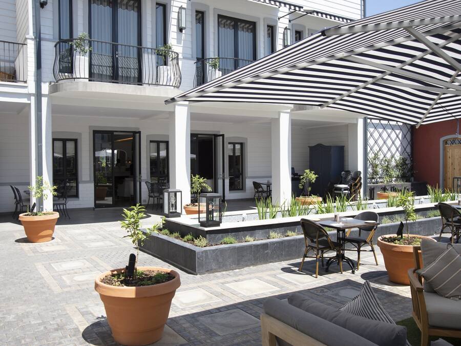 Un patio con mesas al aire libre, plantas en macetas y una zona cubierta con toldo a rayas.