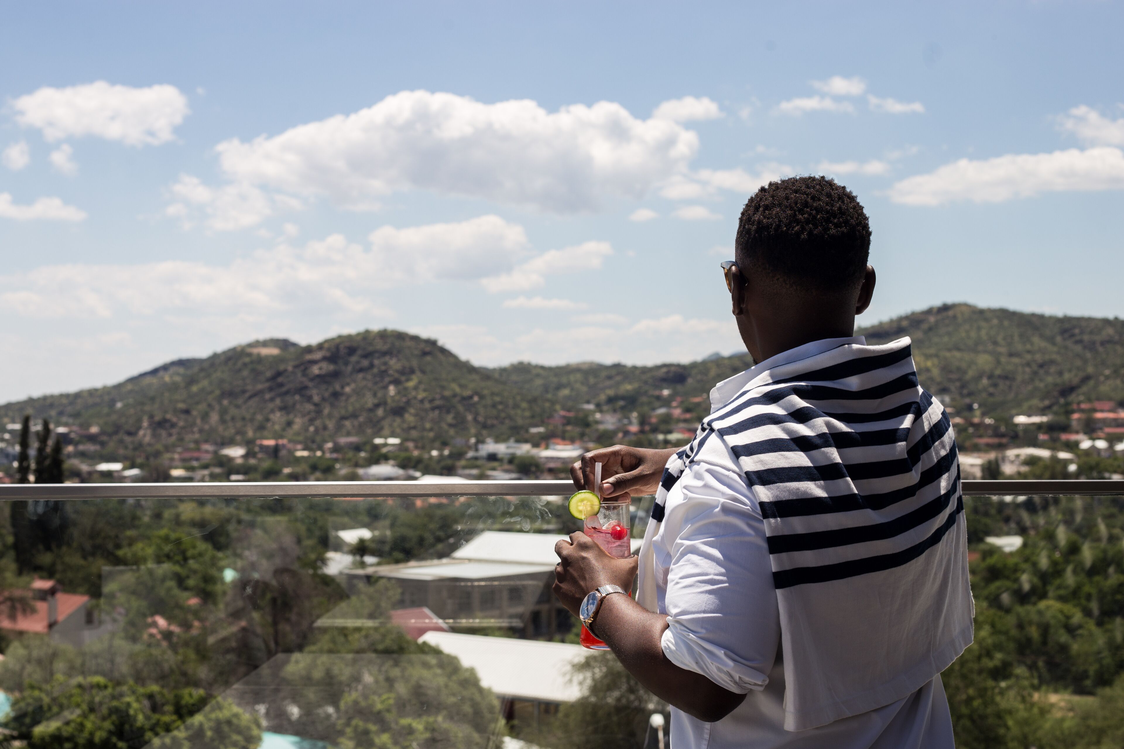 Una persona sosteniendo una bebida con vistas a un pueblo y colinas al fondo.
