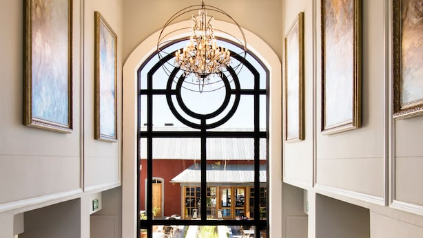 Un vaste hall d’entrée avec une grande fenêtre en arc de cercle, des œuvres d’art encadrées accrochées aux murs et un lustre.