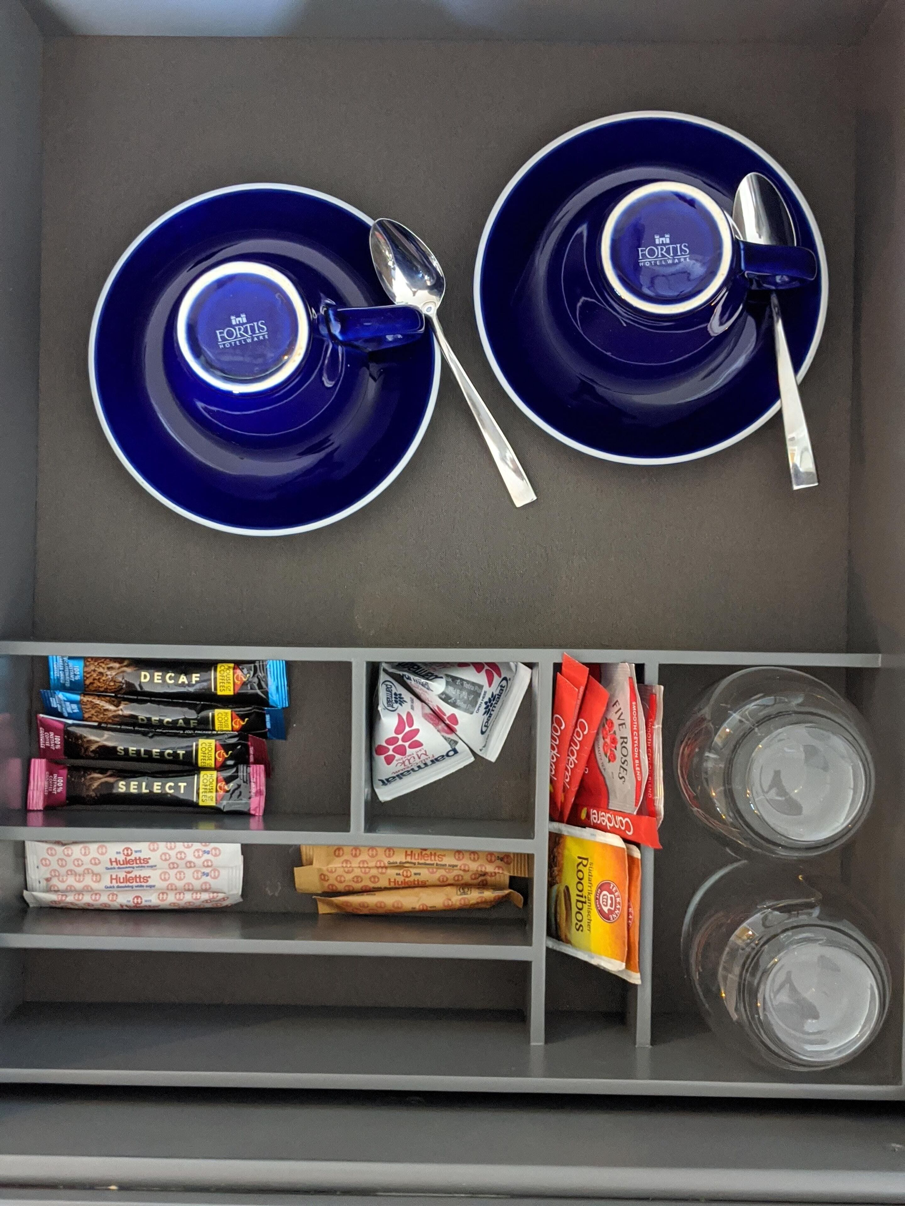 A storage compartment with blue plates and silver spoons, and shelves with various food items and condiments.