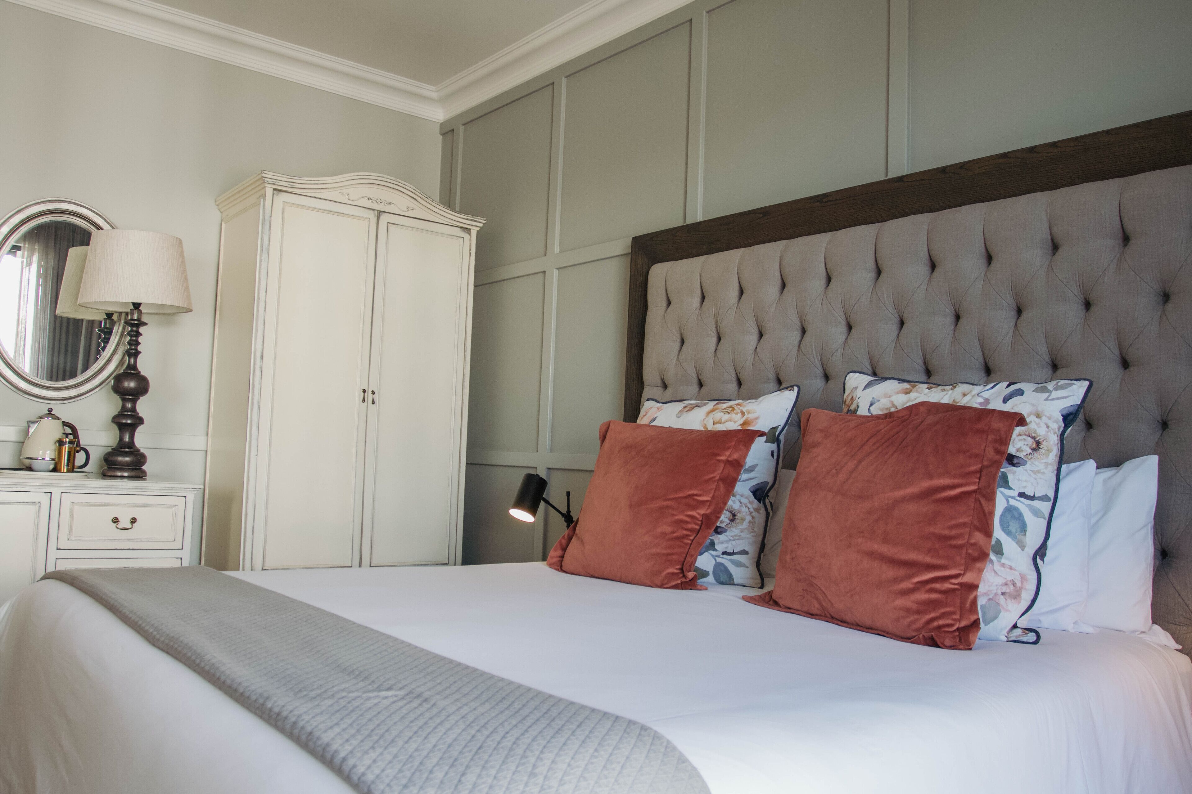 Un dormitorio ordenado con una cama grande, un armario y una mesita de noche con lámpara.