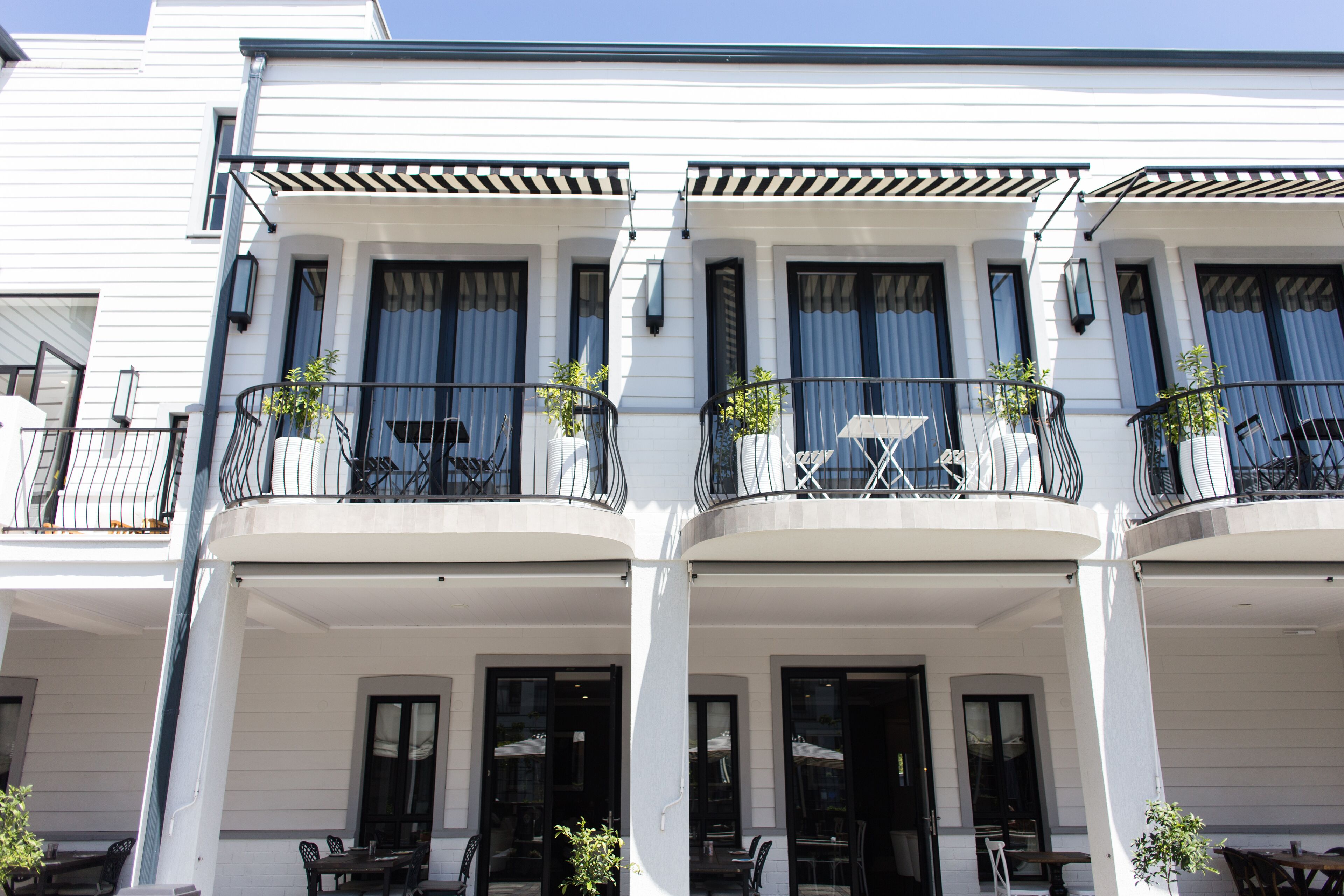 A white building with multiple balconies, each with outdoor seating and potted plants.
