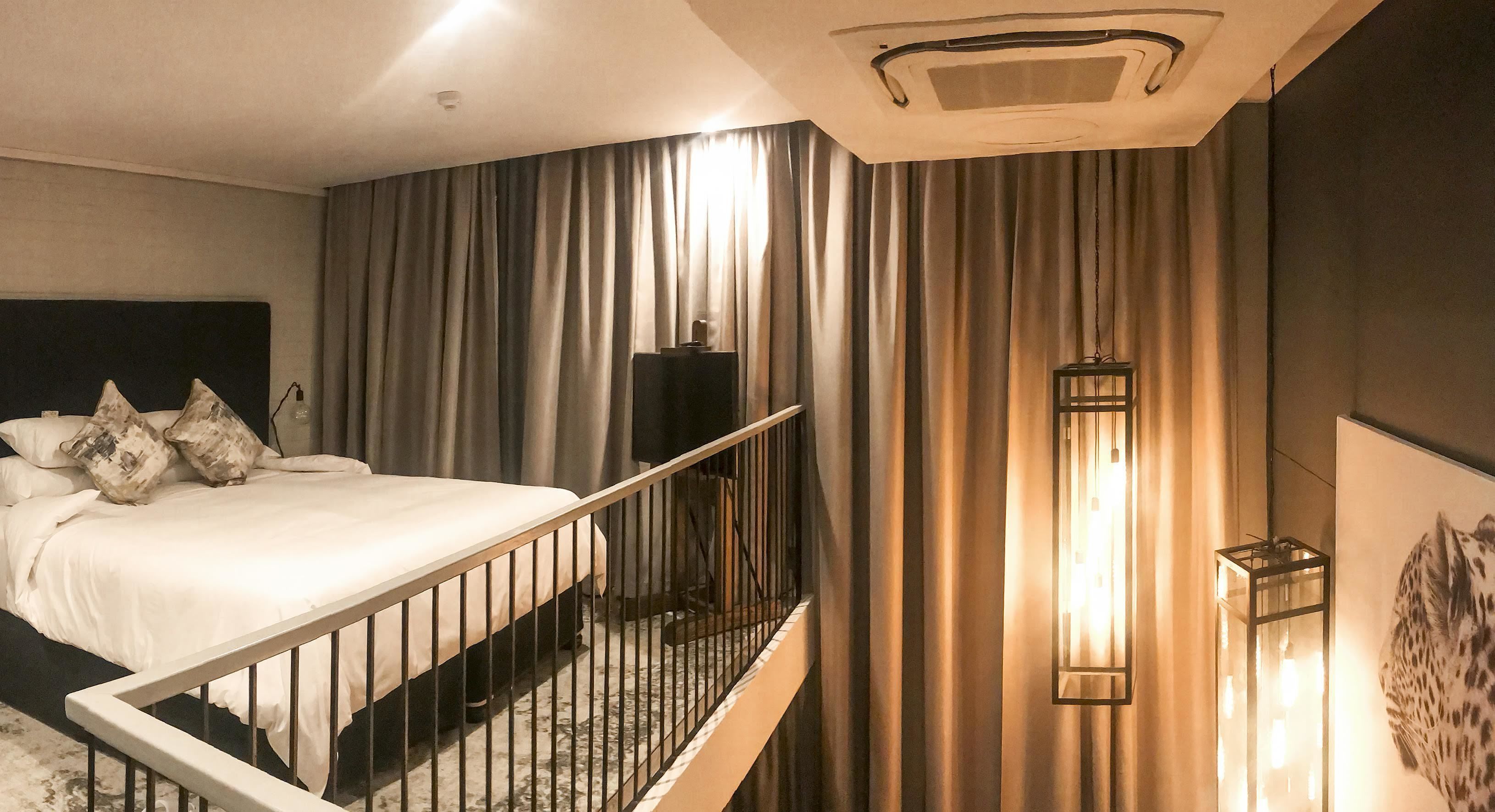 Camera d'albergo con un letto, tende, una ringhiera, un punto luce a parete e una bocchetta di ventilazione al soffitto.