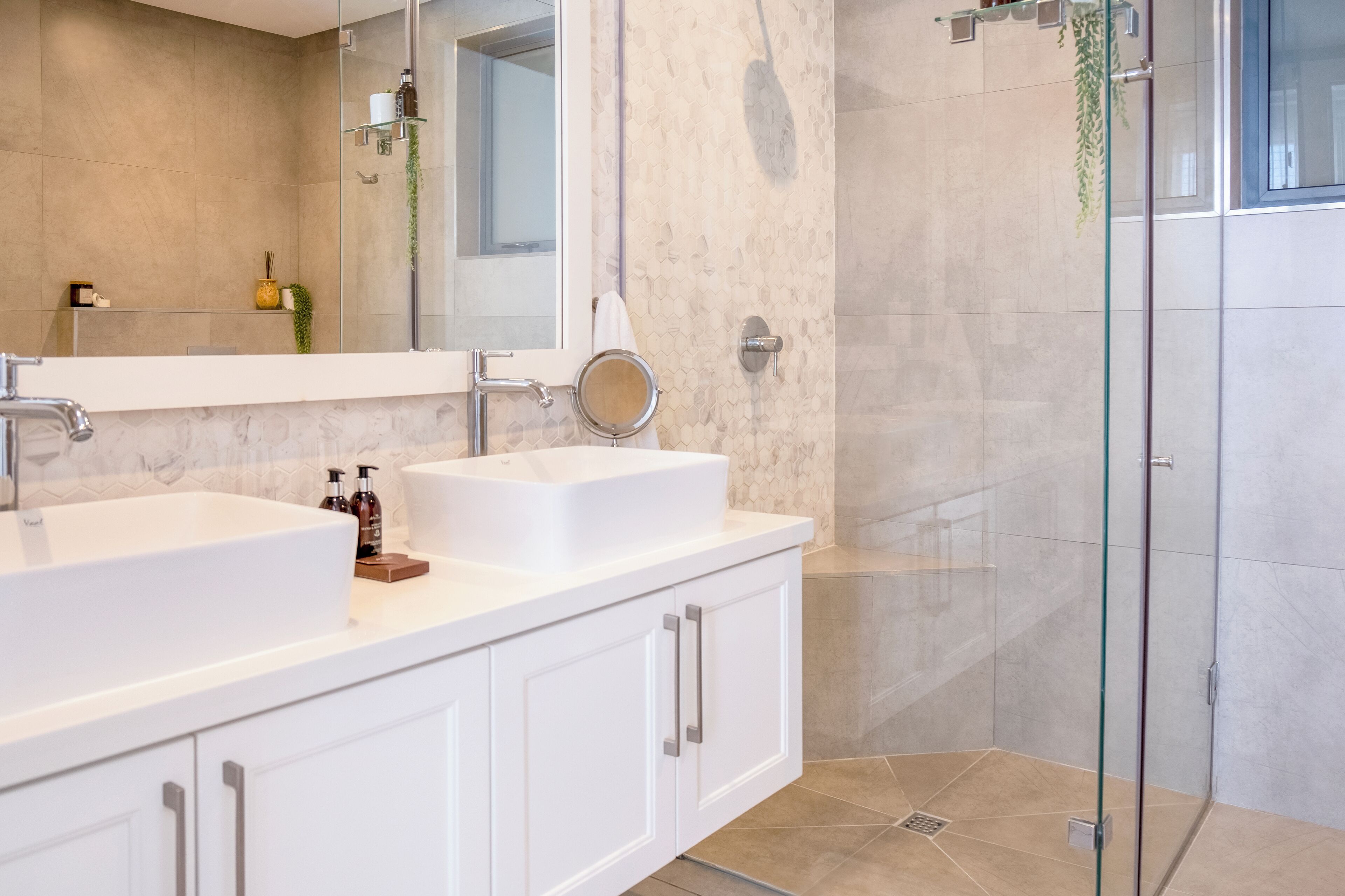 A modern bathroom with two sinks, a large mirror, and a glass shower enclosure.
