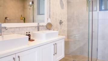 A modern bathroom with two sinks, a large mirror, and a glass shower enclosure.