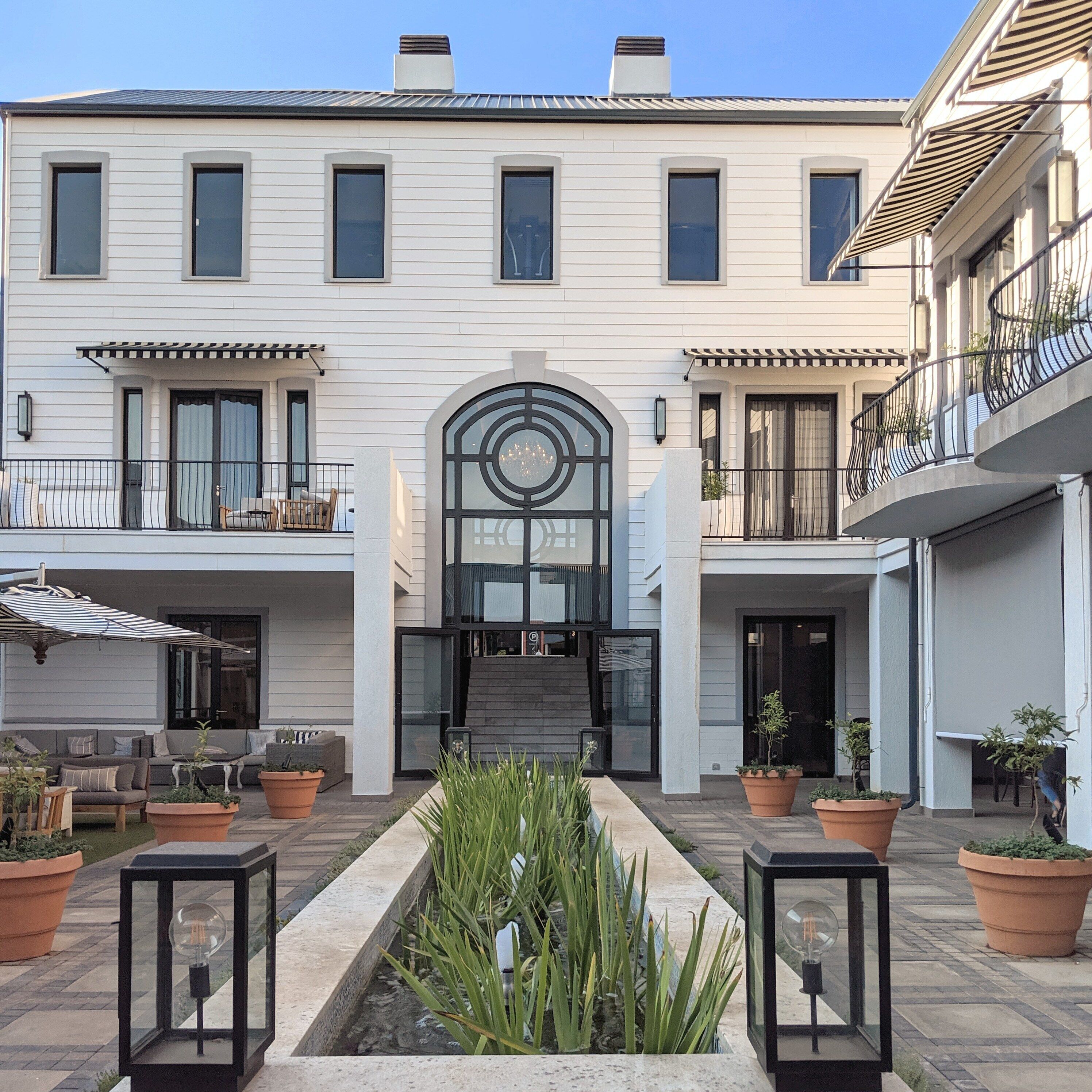 A building with a central entrance, two balconies, and a courtyard with planters and outdoor seating.