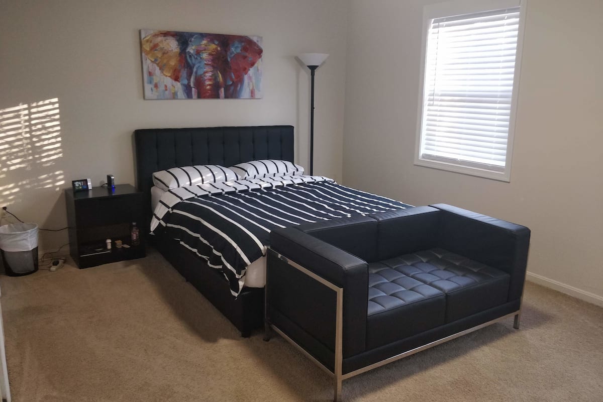 A bedroom with a bed, bedside table, lamp, and a painting on the wall.