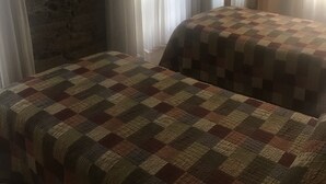 Ein Zimmer mit kariertem Bettbezug, Steinwand und transparenten Vorhängen.