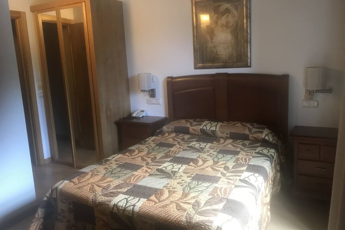 A hotel room with a bed, a nightstand with a lamp, a phone, and a painting on the wall.