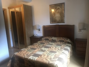 Una habitación de hotel con una cama, una mesita de noche con lámpara, un teléfono y un cuadro en la pared.