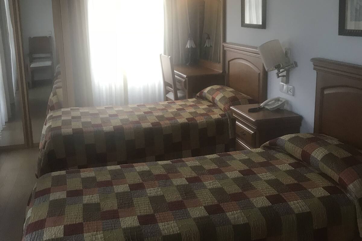 A hotel room with two beds, a desk, a chair, a mirror, and a nightstand.