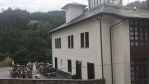 Ein Gebäude mit einer Steinfassade und zahlreichen Fenstern. Eine Gruppe Personen sitzt auf der Terrasse.