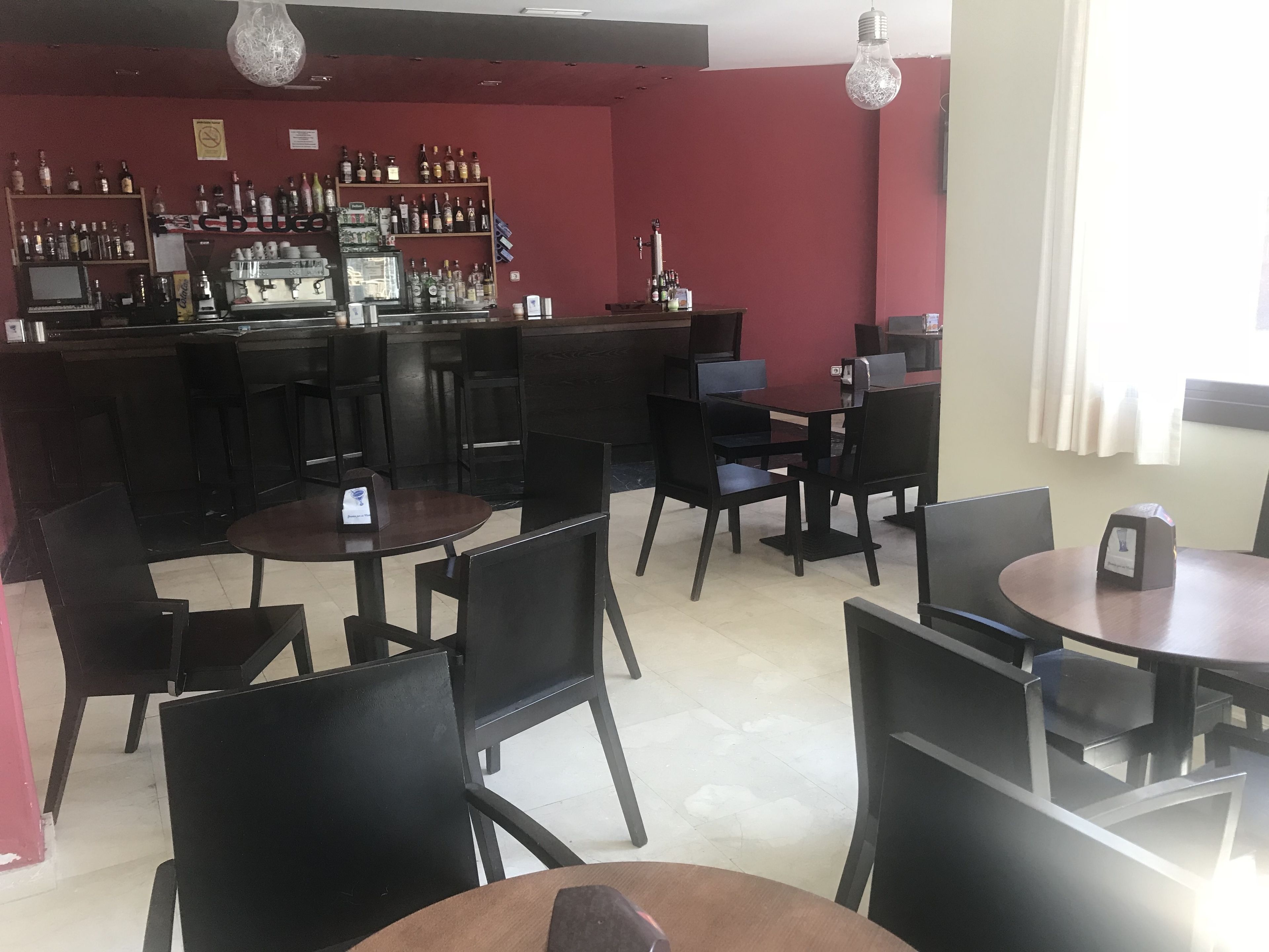 A bar area with multiple tables and chairs, a bar counter with various bottles, and a red wall.