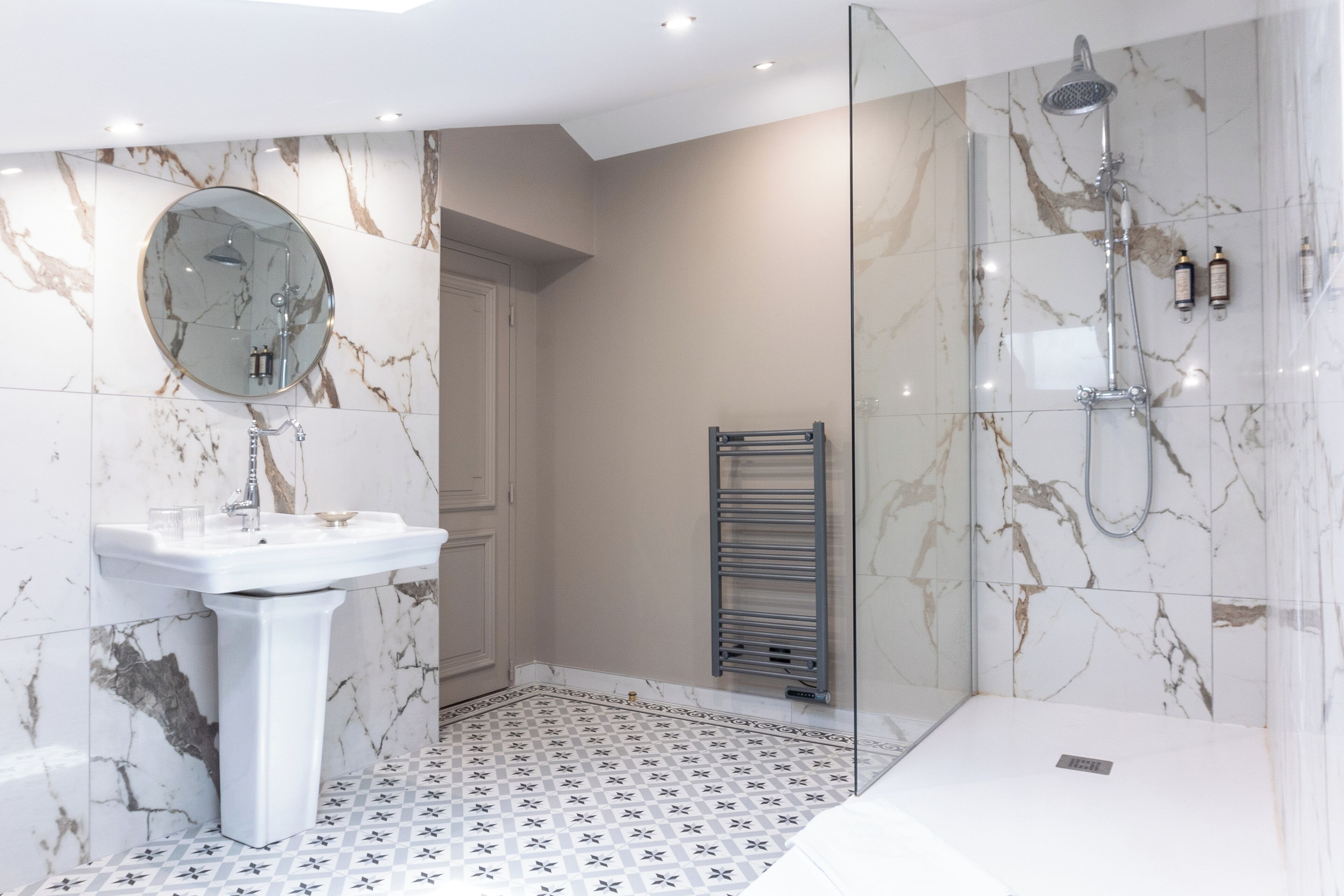 Un baño moderno con piso de mármol, lavamanos blanco, ducha con mampara de vidrio y toallero.
