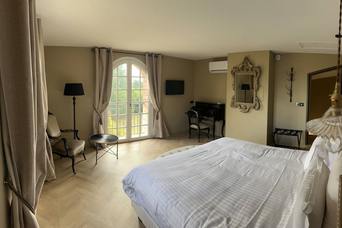 Ein Schlafzimmer mit einem großen Bett, einem Schreibtisch, einem Stuhl und einem Fenster mit Vorhängen.