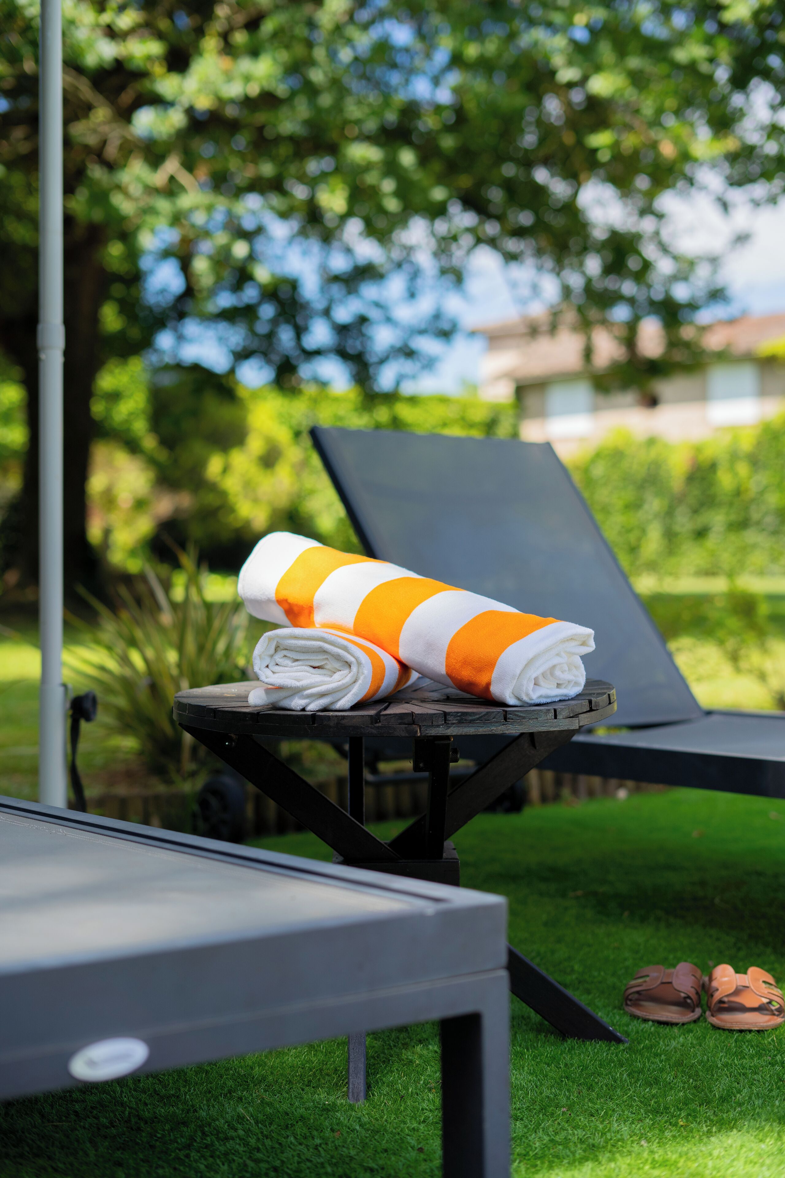 A lounge chair with a towel and a pair of sandals on the grass.