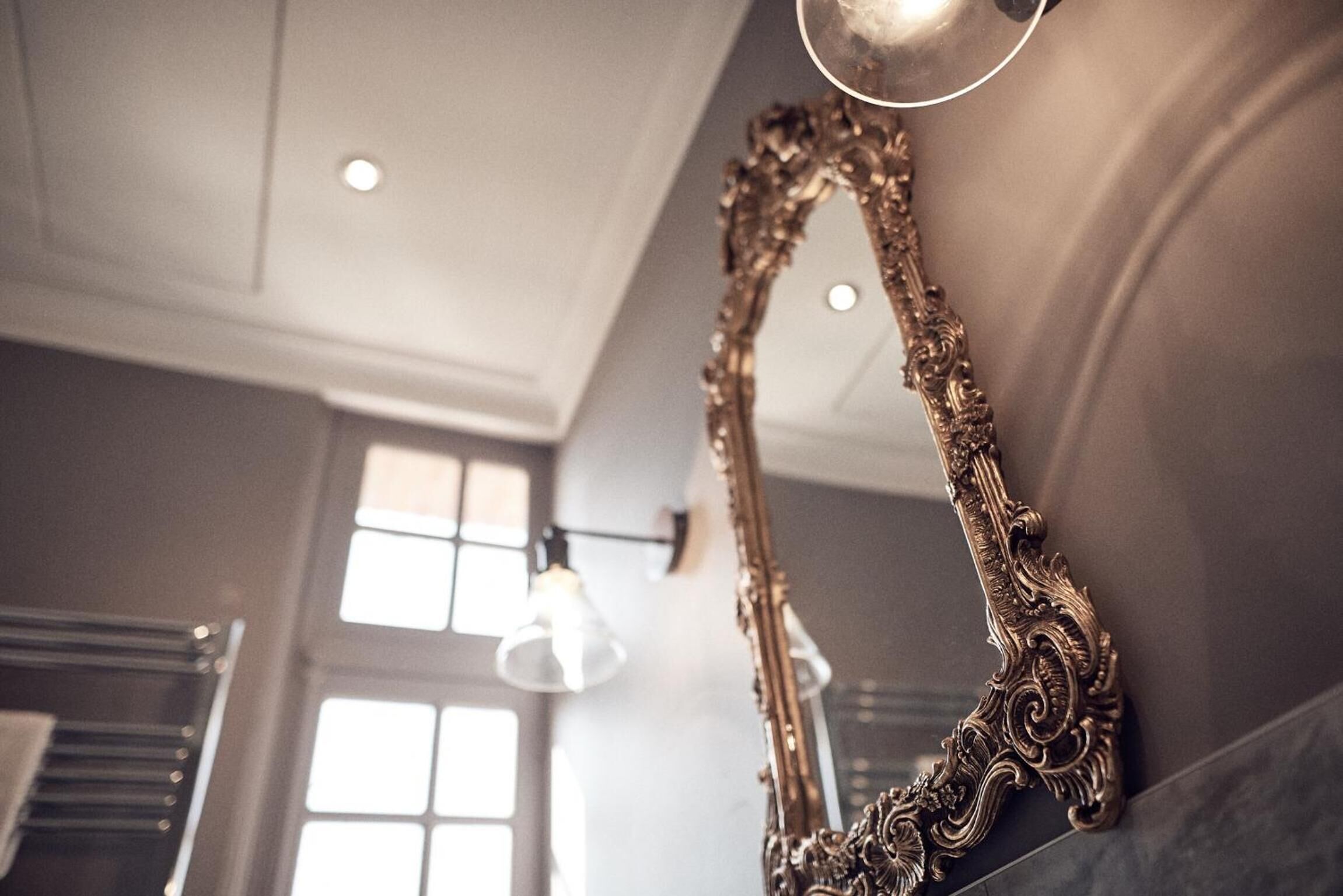 An ornate mirror with intricate designs, a modern light fixture, and a window with multiple panes.