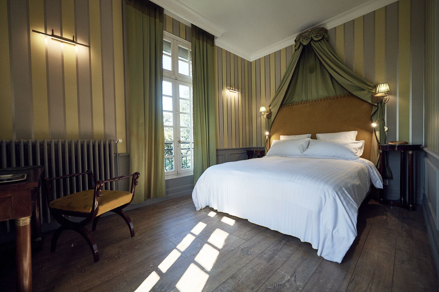 A bedroom with a large bed, a chair, a radiator, and a window with curtains.