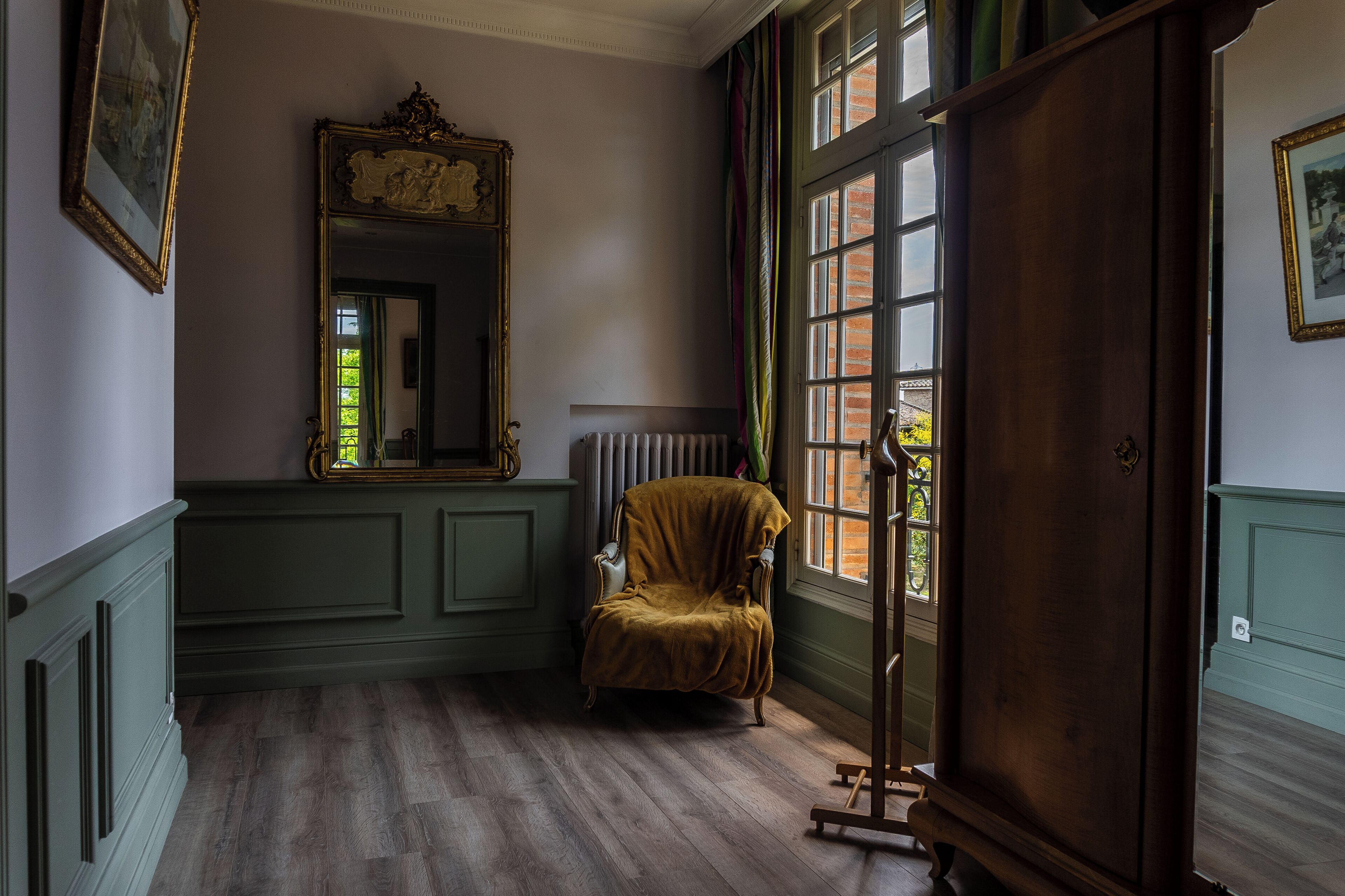 Ein Zimmer mit einem großen Spiegel, einem Sessel, einer Heizung und einem Fenster mit Blick auf Grünflächen.