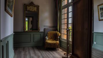 Ein Zimmer mit einem großen Spiegel, einem Sessel, einer Heizung und einem Fenster mit Blick auf Grünflächen.