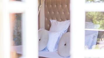 Een bed met een gestuikt hoofdbord, wit beddengoed en een bruine plaid.