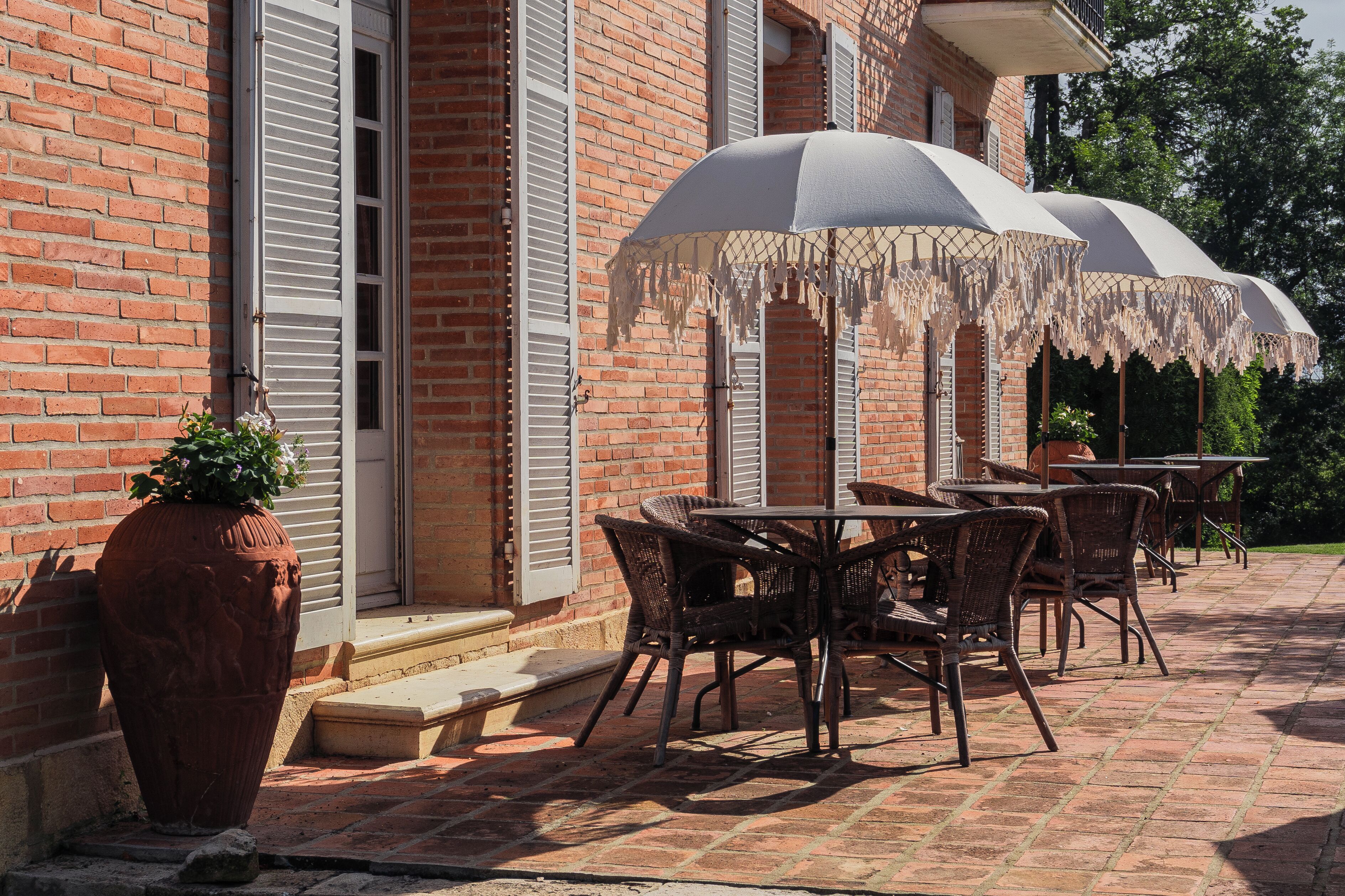 Eine Terrasse im Freien mit Ziegelmauern, weißen Fensterläden und Korbmöbeln.