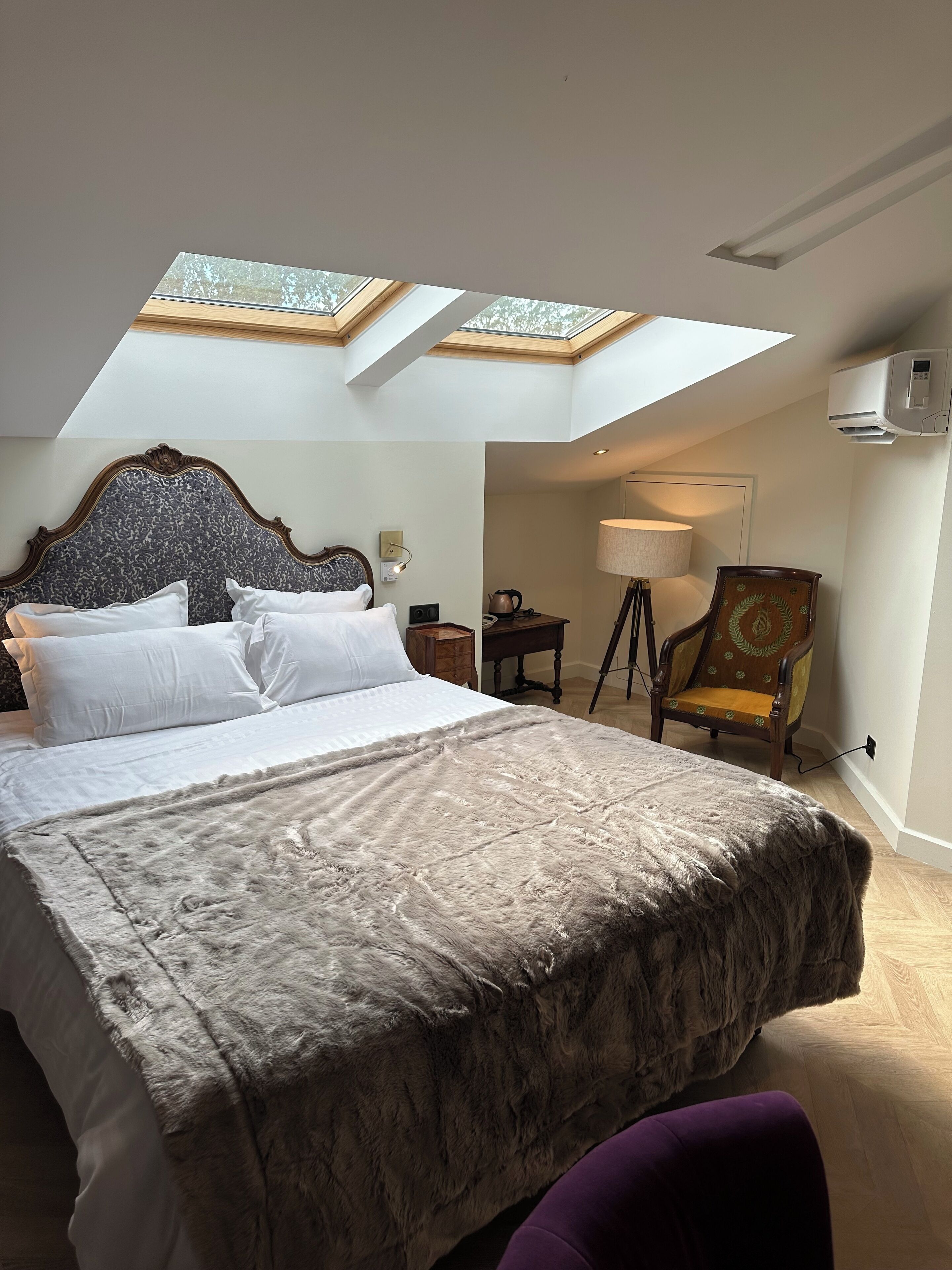 Une chambre avec un grand lit, une lucarne, une chaise et une lampe.