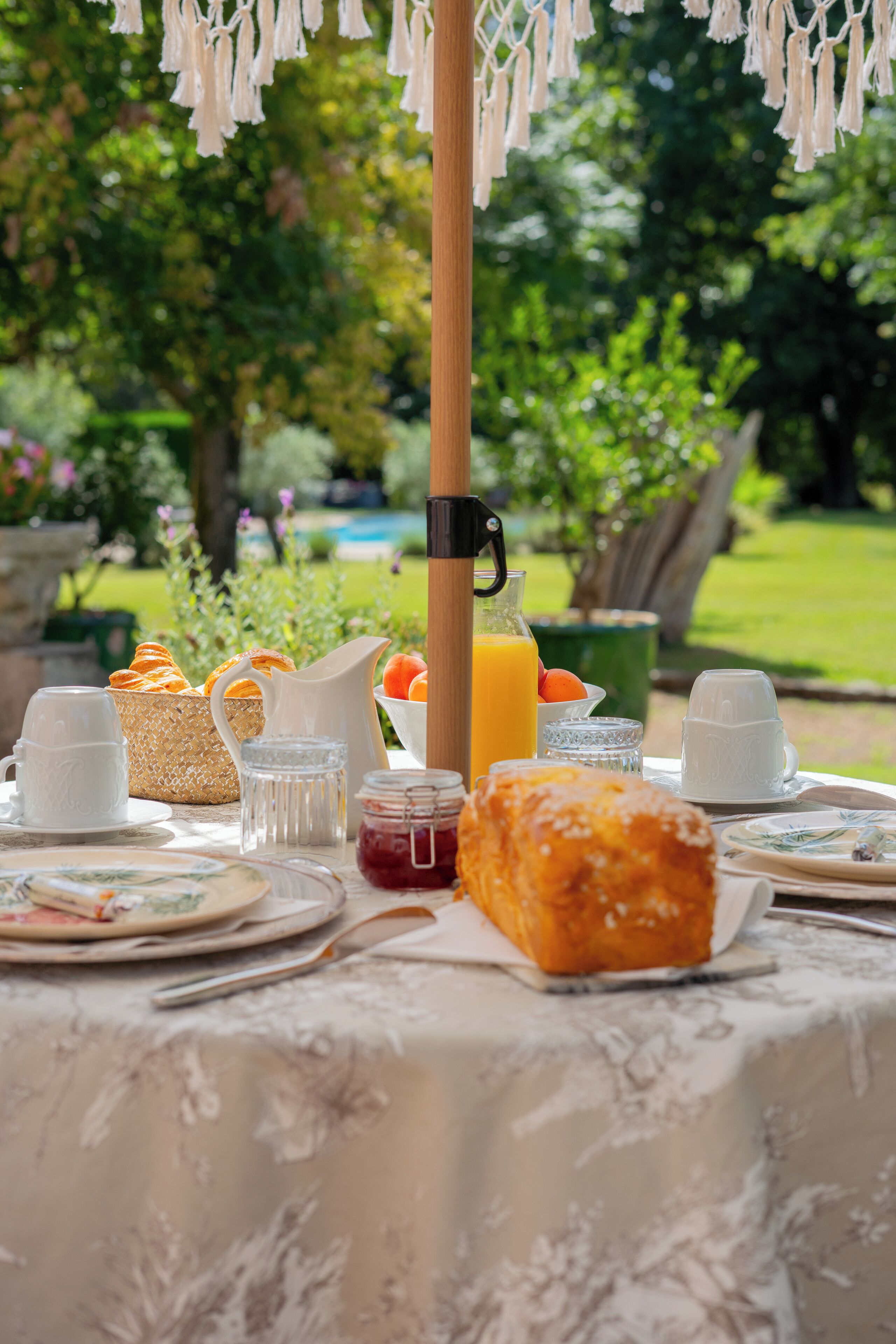 Une table de petit-déjeuner installée à l’extérieur, avec divers aliments, une carafe de jus d’orange et un verre d’eau.