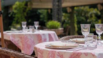 Un espace extérieur aménagé pour les repas, avec des chaises et des tables en osier recouvertes de nappes à motifs floraux.