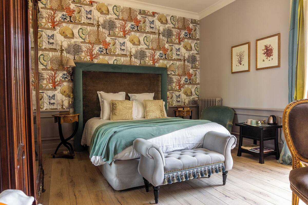 Ein Schlafzimmer mit einem großen Bett, einem grünen Polsterstuhl, einem kleinen Tisch und einer Wand mit Muster.