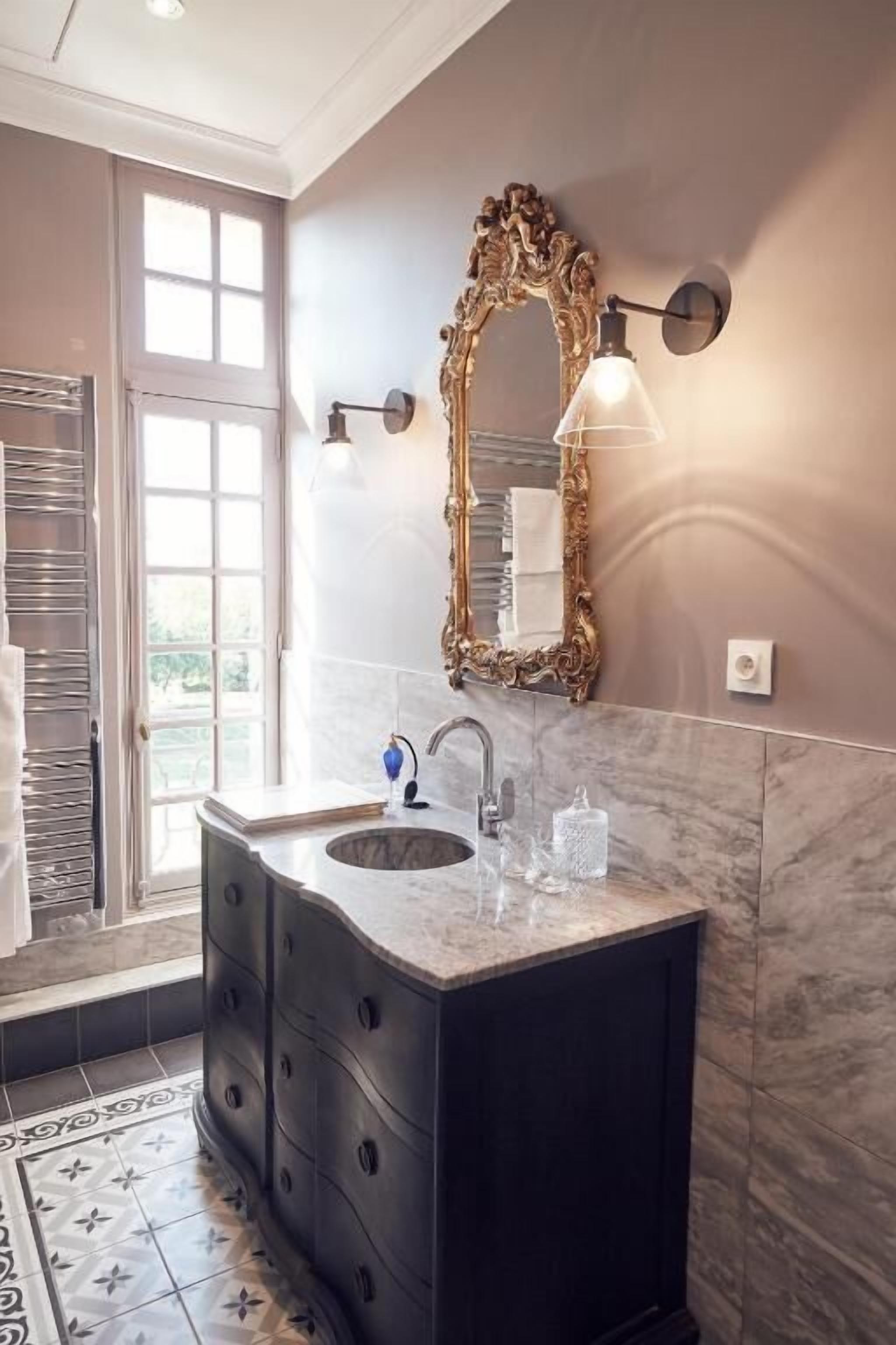 Une salle de bain dotée d’un meuble-lavabo à deux vasques, d’un grand miroir décoratif et d’un sol à motifs.