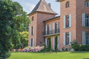 Un edifici gran de maó amb una torre, persianes blanques i un balcó.