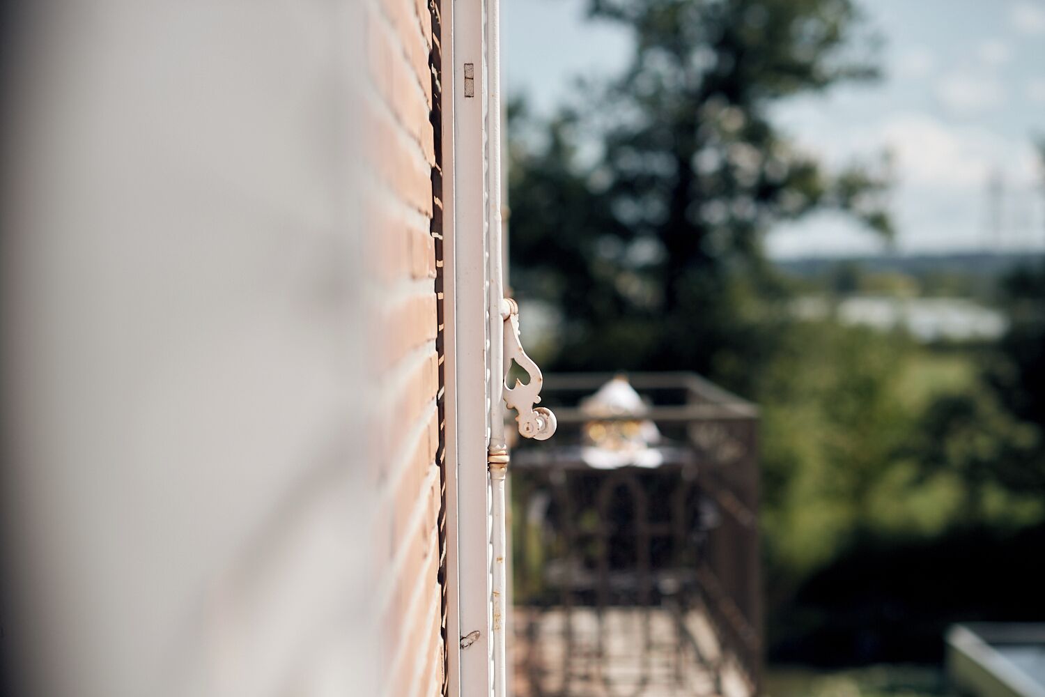Une vue à travers une porte entrouverte, avec un mur de briques et un portail en métal donnant sur un jardin.
