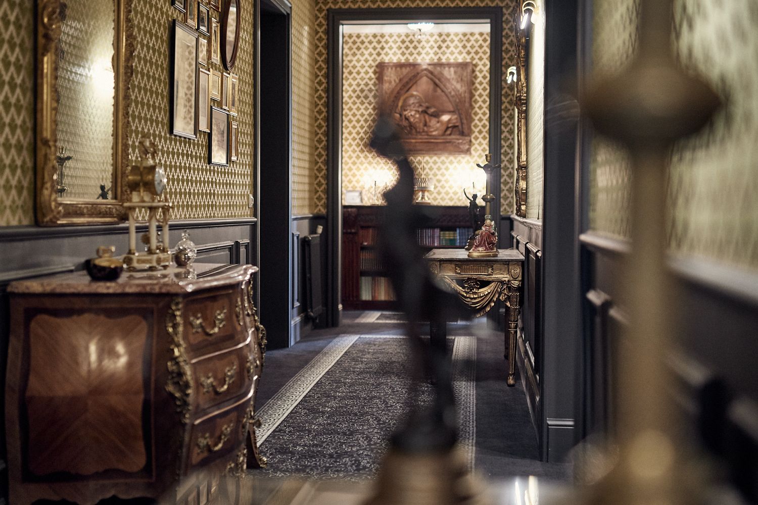 A grand hallway with ornate wall decorations, a large mirror, and a statue on a pedestal.