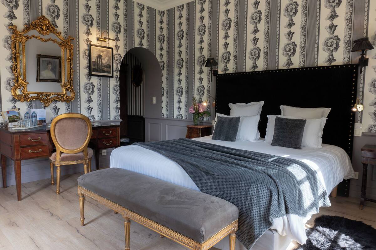 Ein Schlafzimmer mit einem großen Bett, einem Schminktisch mit Spiegel, einem Schreibtisch und einer Bank.